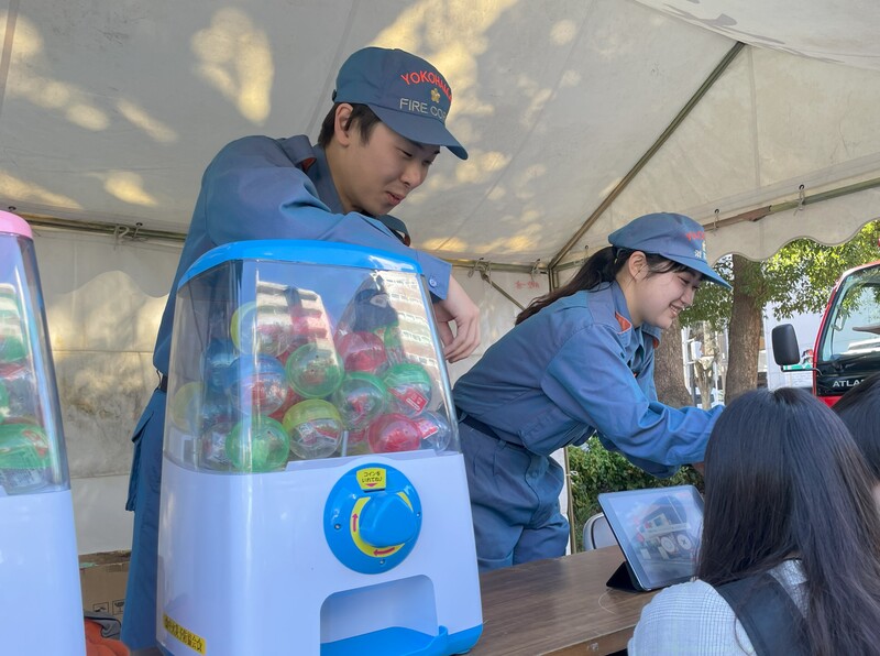 子供にガチャガチャを渡す消防団員
