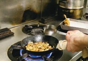 西洋料理の調理人がフライパンで食材を炒める様子