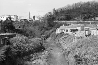 帷子川を挟んで左に稲荷社、右に横浜輸出スカーフ施設協同組合。協同組合の背後の道路は国道16号線であ。